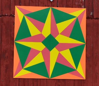 Barn quilt on a red barn. Barn quilt depicts compass star with orange and green border with yellow a