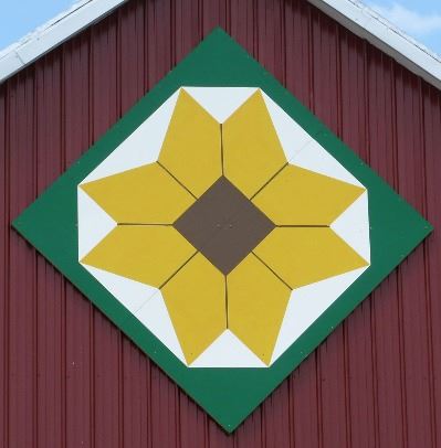 Brown-Eyed Susan on a barn quilt in a diamond pattern on a red barn. The Brown-Eyed Susan is surroun