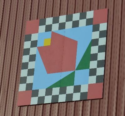 Barn quilt on the side of a red barn. The pattern is of a red tulip in the center with a blue backgr